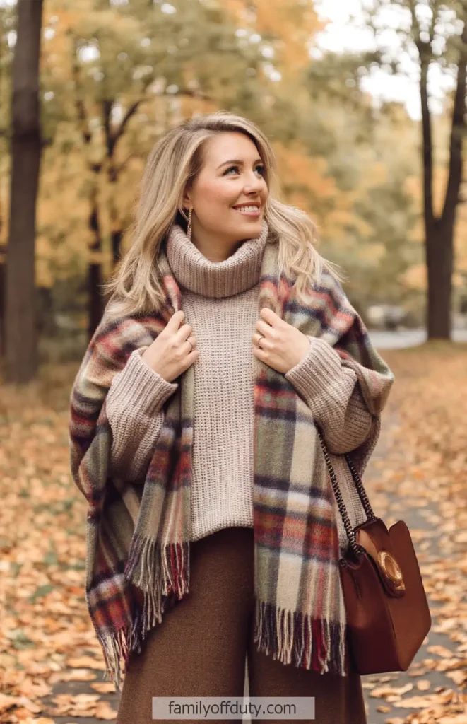 Woman in cozy fall outfit with plaid scarf, walking in autumn park with colorful leaves.