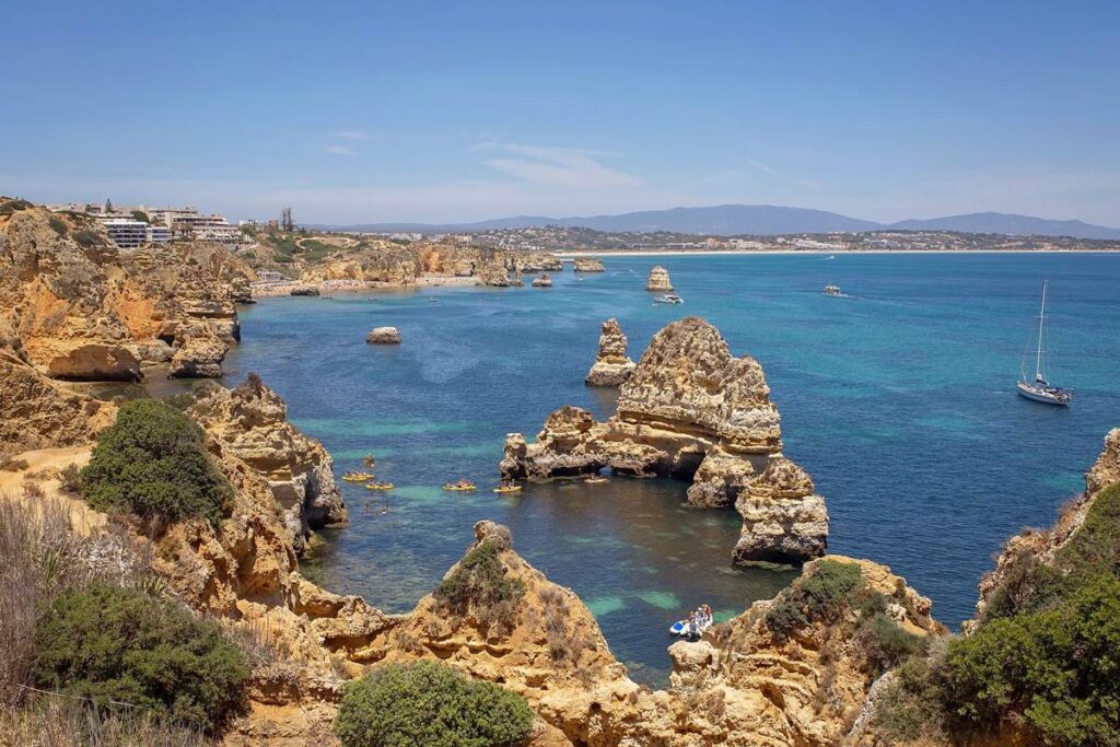 Stunning Algarve coastline with rocky cliffs, clear blue water, and sailboats under a sunny sky. Perfect travel destination.