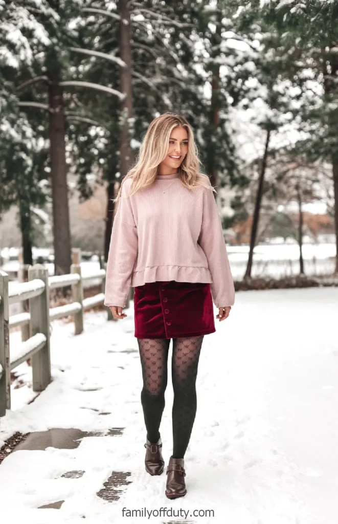 Woman in winter fashion walking on snowy path with trees in background.