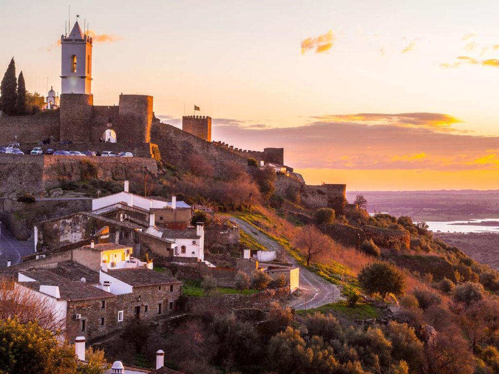 Sunset view of Monsaraz medieval castle and village in Portugal, with vibrant sky and scenic landscape.