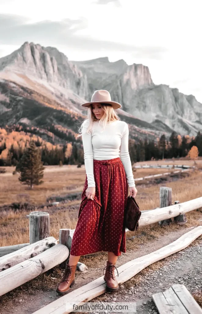 Woman in stylish fall outfit poses with mountains in background.