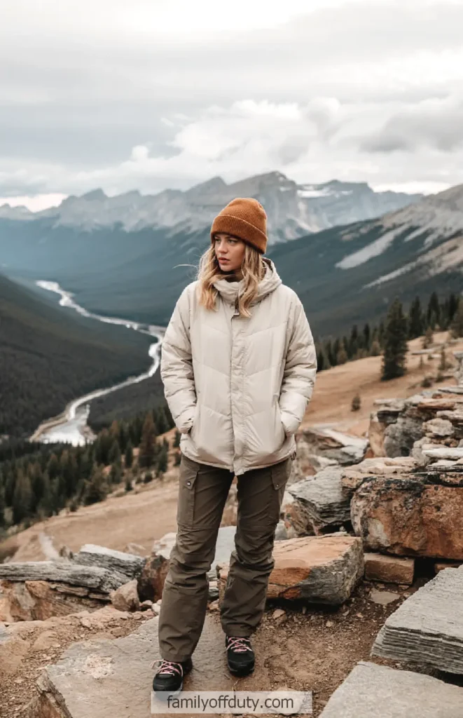 Woman in winter clothing standing on a mountain overlook with a winding river and forested valley below.