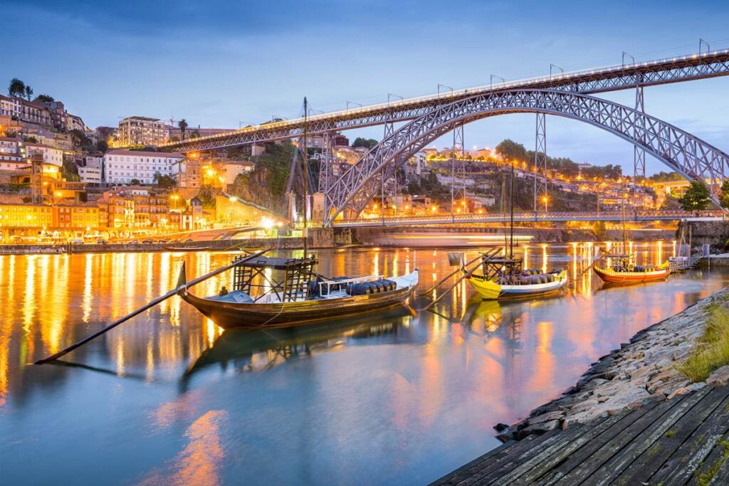 Scenic view of Porto, Portugal at dusk with traditional boats and illuminated architecture reflecting on the Douro River.