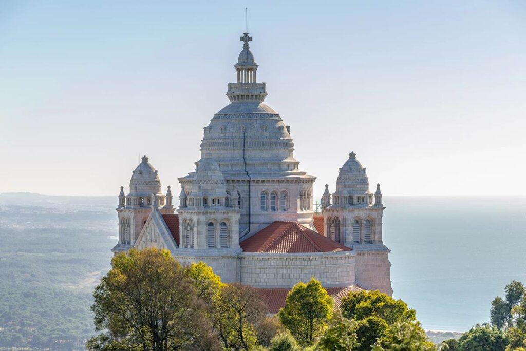 Majestic basilica with ornate domes overlooking lush forests and ocean, set against a clear blue sky.