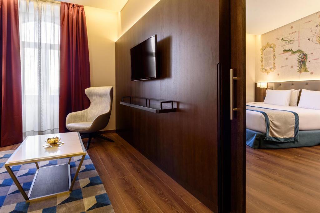 Modern hotel suite with cozy seating, flat-screen TV, elegant decor, and a comfy bed, perfect for relaxation.