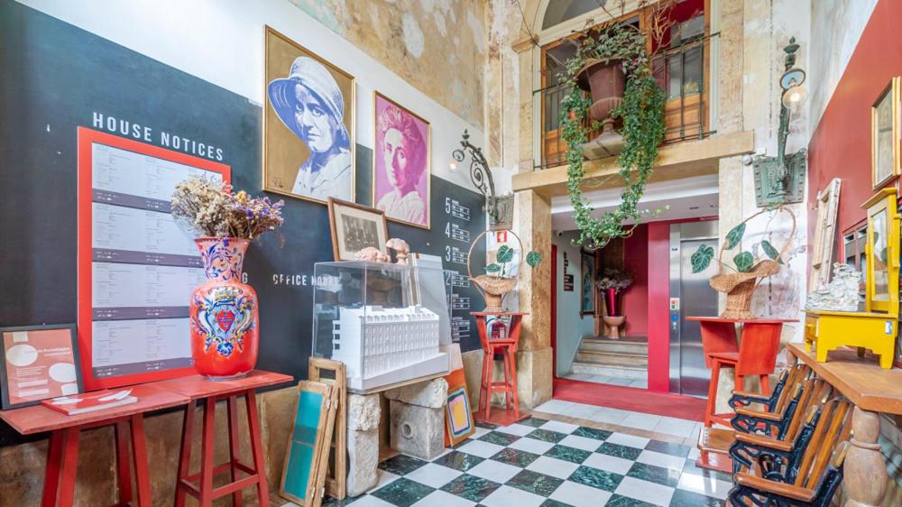 Colorful lobby with vintage decor, checkered floor, potted plants, and artistic portraits on the wall.