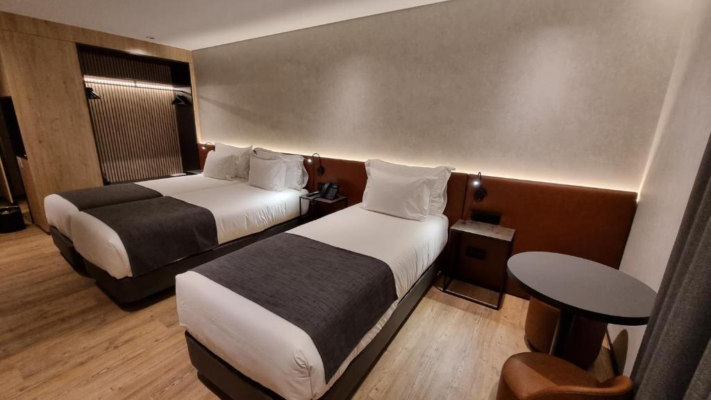 Modern hotel room with two beds, ambient lighting, wooden floor, and a small table, offering a cozy and luxurious stay.