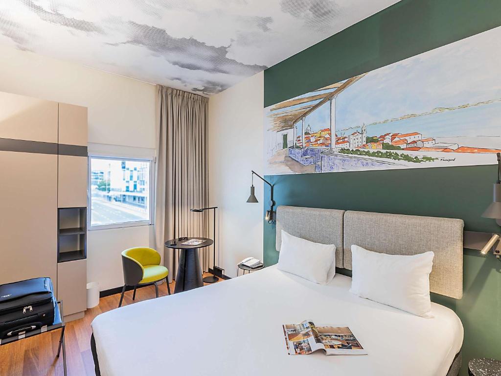 Modern hotel room with a cozy bed, artistic wall mural, and natural light from a window.