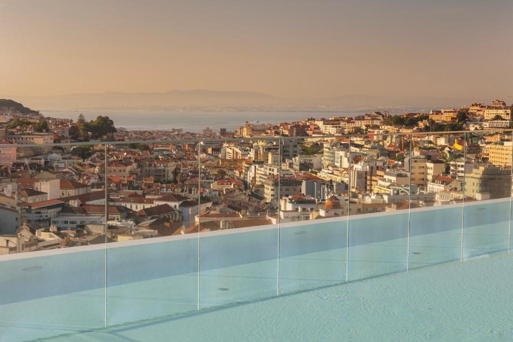 Rooftop infinity pool overlooking a scenic cityscape at sunset, with distant hills and a calm sky.
