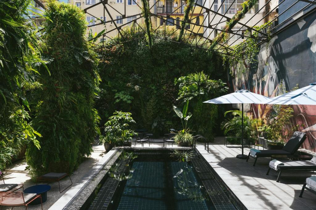 Lush green courtyard with pool, lounge chairs, umbrellas, and vertical gardens in urban setting.