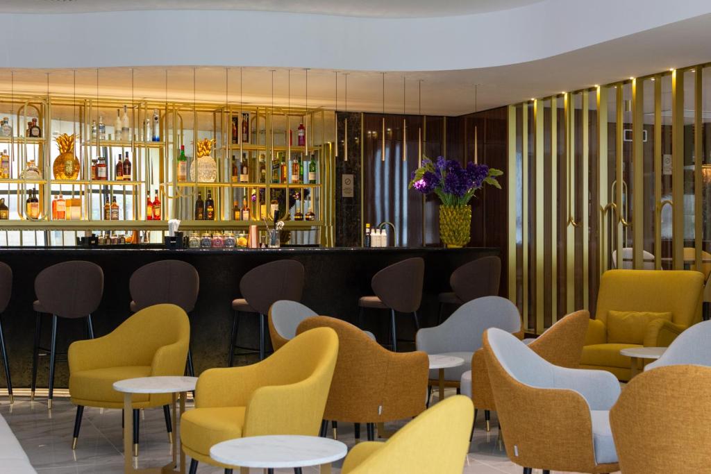 Modern hotel bar lounge with stylish yellow and gray seating, elegant decor, and a well-stocked backlit bar.