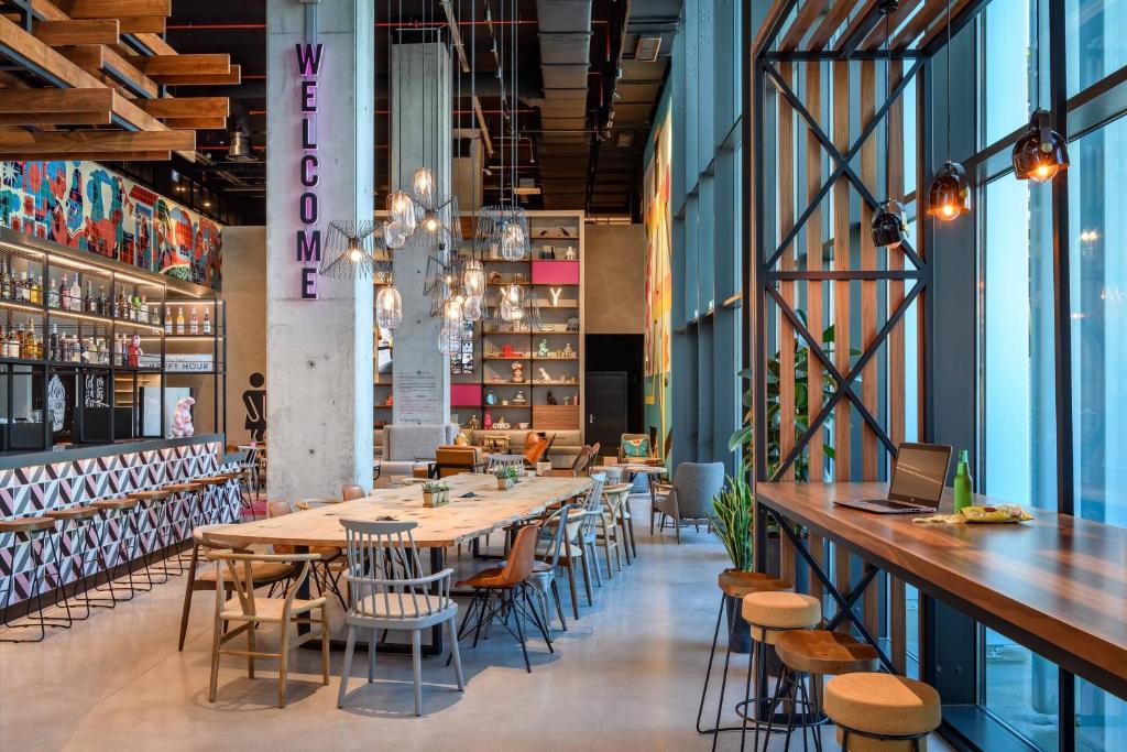 Modern cafe interior with vibrant decor, long wooden tables, and a cozy seating area under hanging lights.