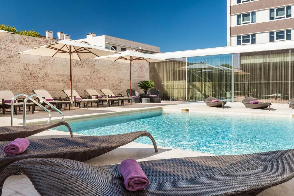 Modern hotel pool with sun loungers and umbrellas, perfect for relaxation under a clear blue sky.