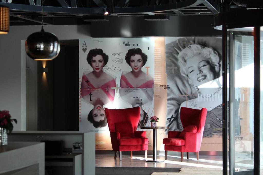 Modern lounge interior with red chairs, artistic wall portraits, and stylish decor elements around a small table.