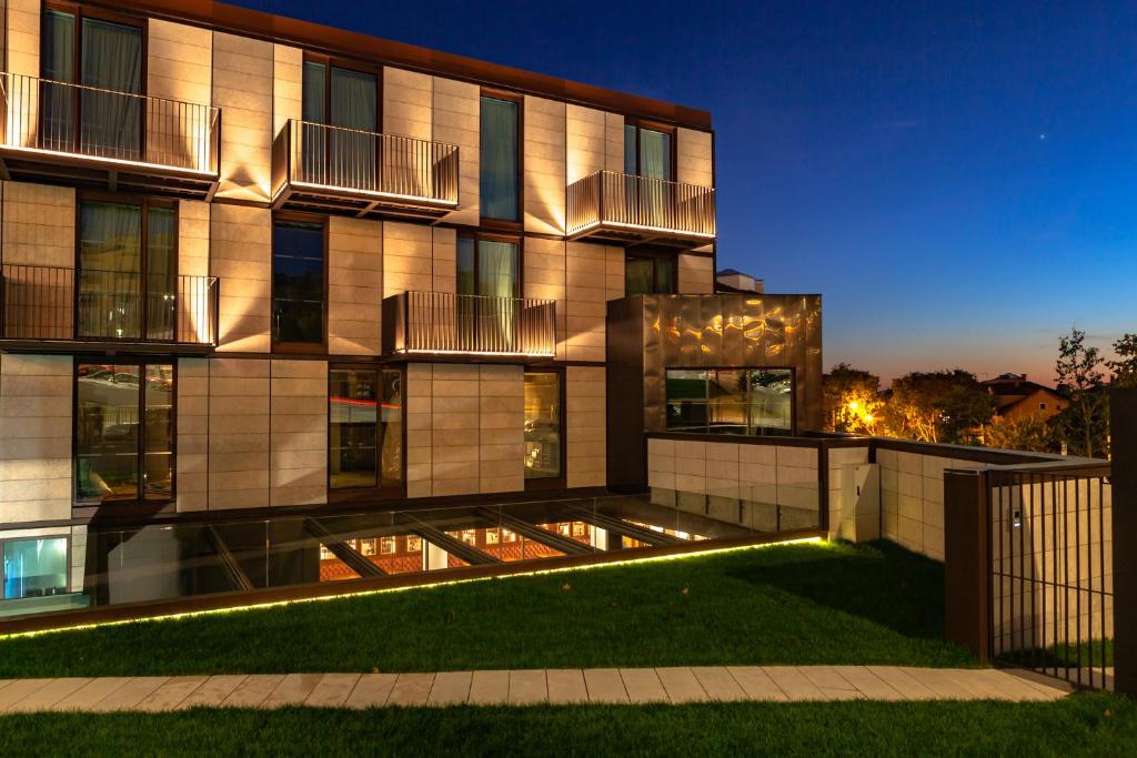 Modern apartment building at dusk with illuminated balconies and a landscaped garden.