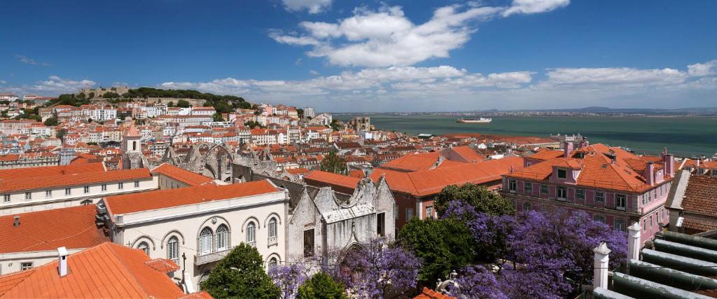 Scenic view of Lisbon's red rooftops with the Tagus River and a ship in the background under a blue sky.