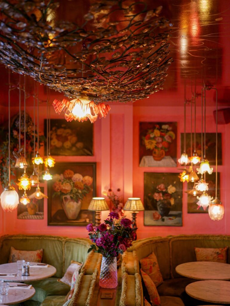 Cozy pink café interior with floral decor, elegant lighting, and plush seating, creating a warm and inviting atmosphere.