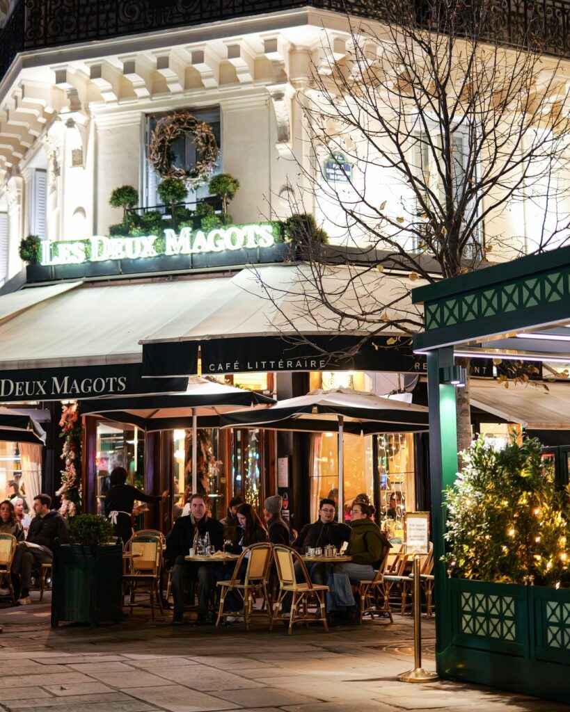 Outdoor dining at a Parisian cafe, Les Deux Magots, with people enjoying an evening meal under a canopy.