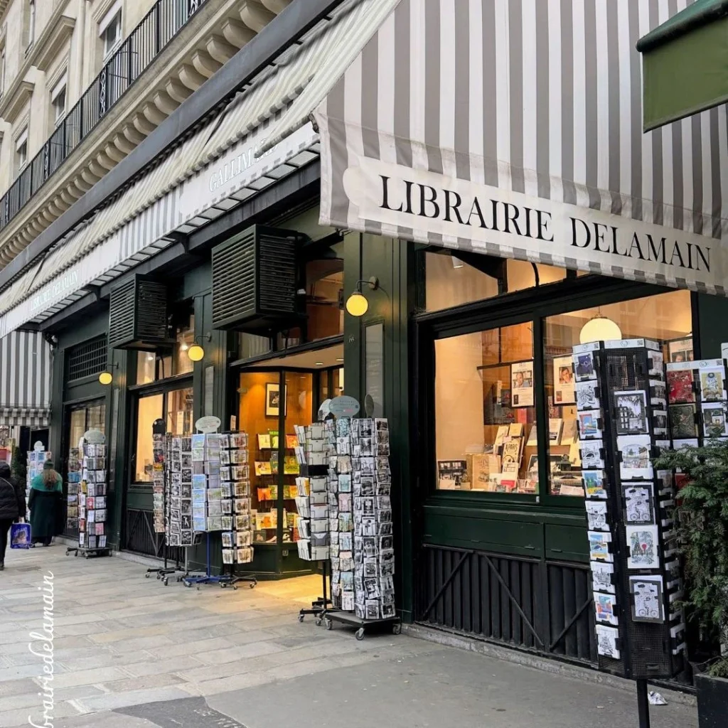 Exterior of Librairie Delamain bookstore with postcard stands in Paris. Cozy, historic shop facade.