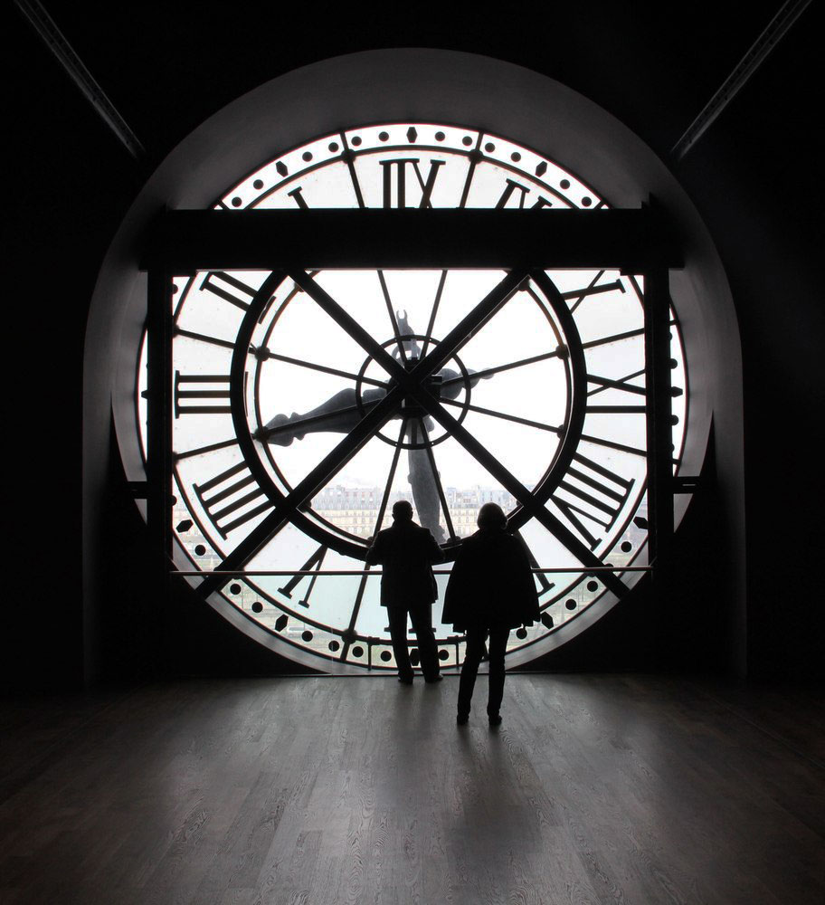 Silhouettes viewing city through large Roman numeral clock face at Musée d'Orsay, Paris.