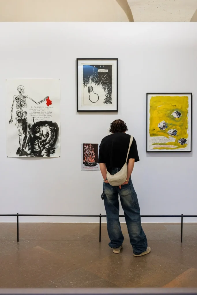 Person viewing diverse art pieces in a gallery exhibition. Casual attire, white wall background.