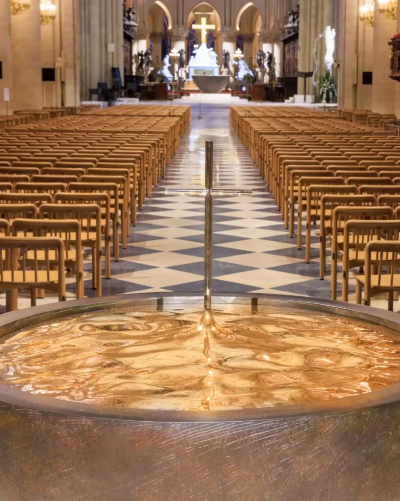 Baptismal font and rows of chairs in a church interior with altar and cross.