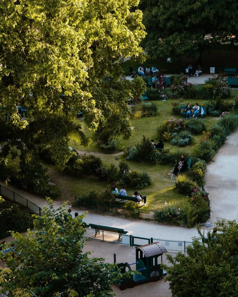 Aerial view of a lush park with people relaxing, green trees, pathways, and a playground area with a small play train.