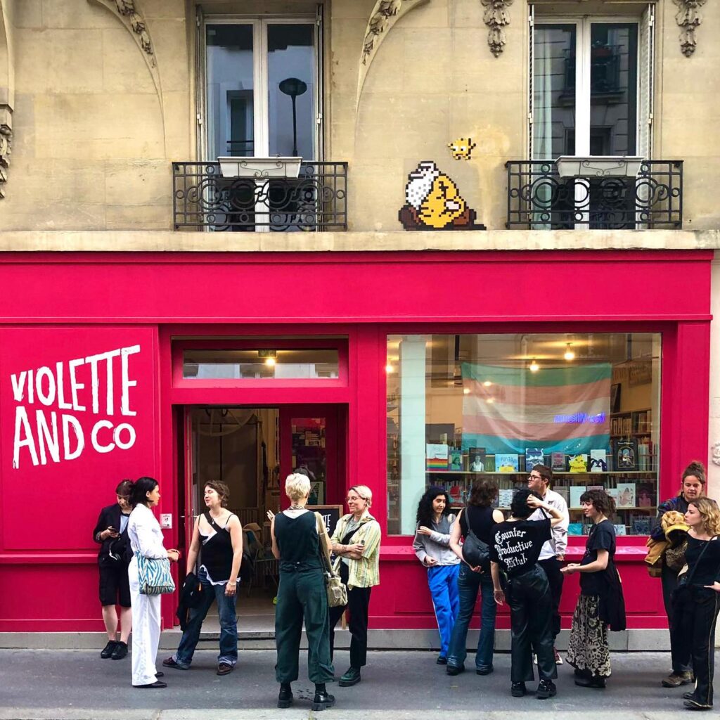 People gather outside the vibrant red Violette and Co bookstore in a lively urban setting.