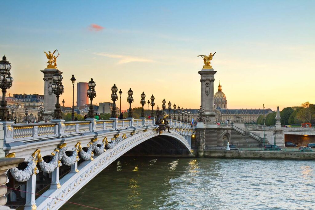 Elegant bridge over the Seine River at sunset with ornate sculptures and intricate lamp posts.