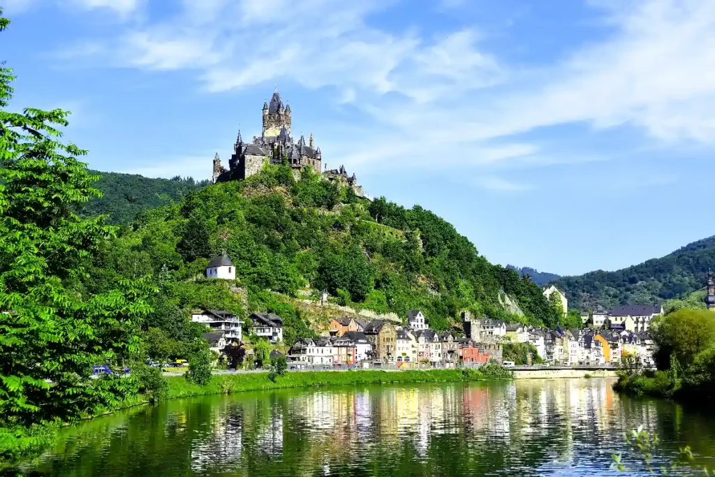 Stunning view of a castle on a hill surrounded by lush greenery and a serene river reflecting the sky. Perfect for travel.