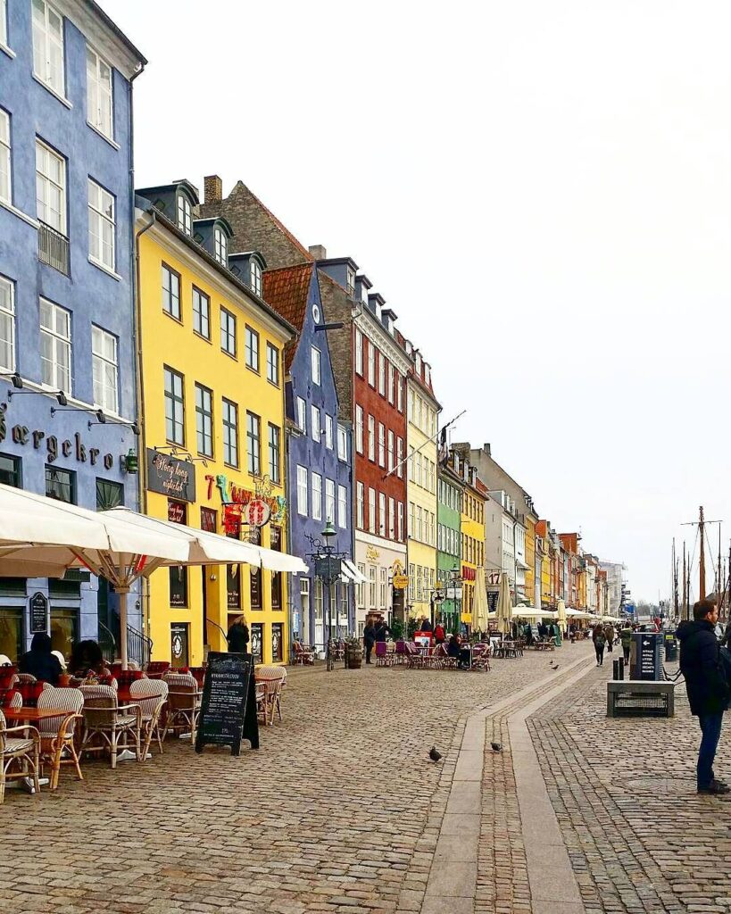 Colorful buildings in Nyhavn, Copenhagen with outdoor cafés and cobblestone street, creating a vibrant urban scene.