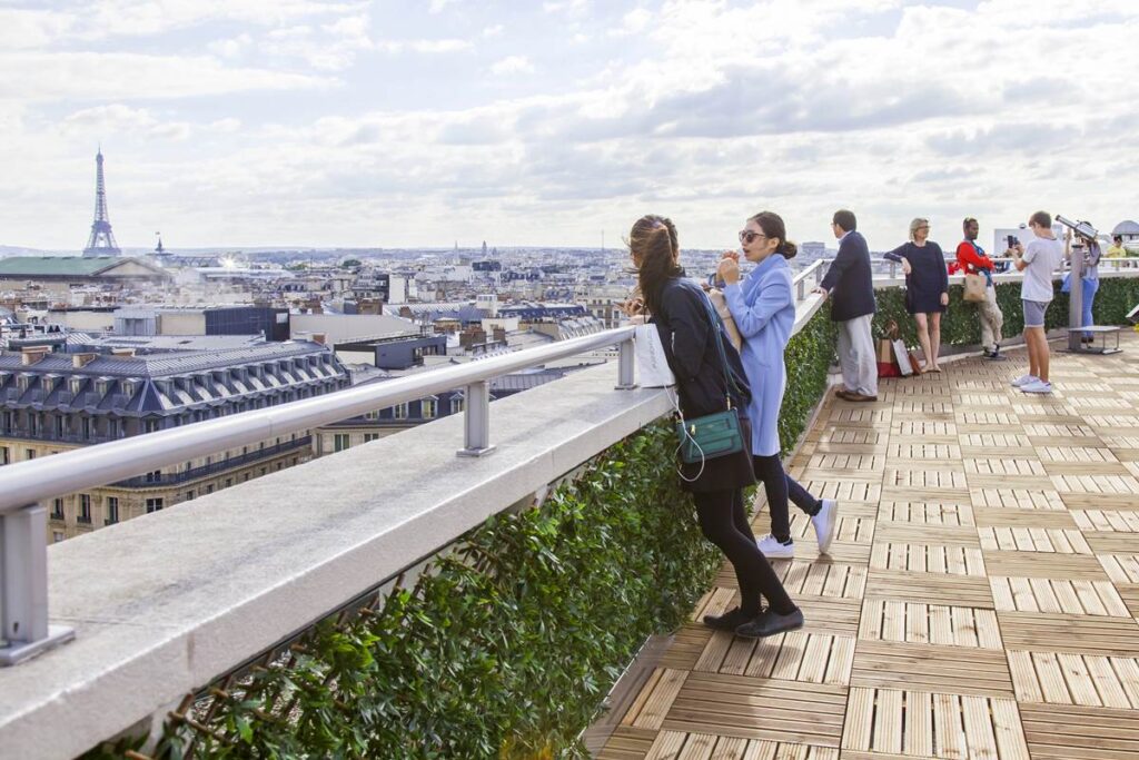 People enjoying a rooftop view of Paris, with the Eiffel Tower in the distance under a partly cloudy sky.