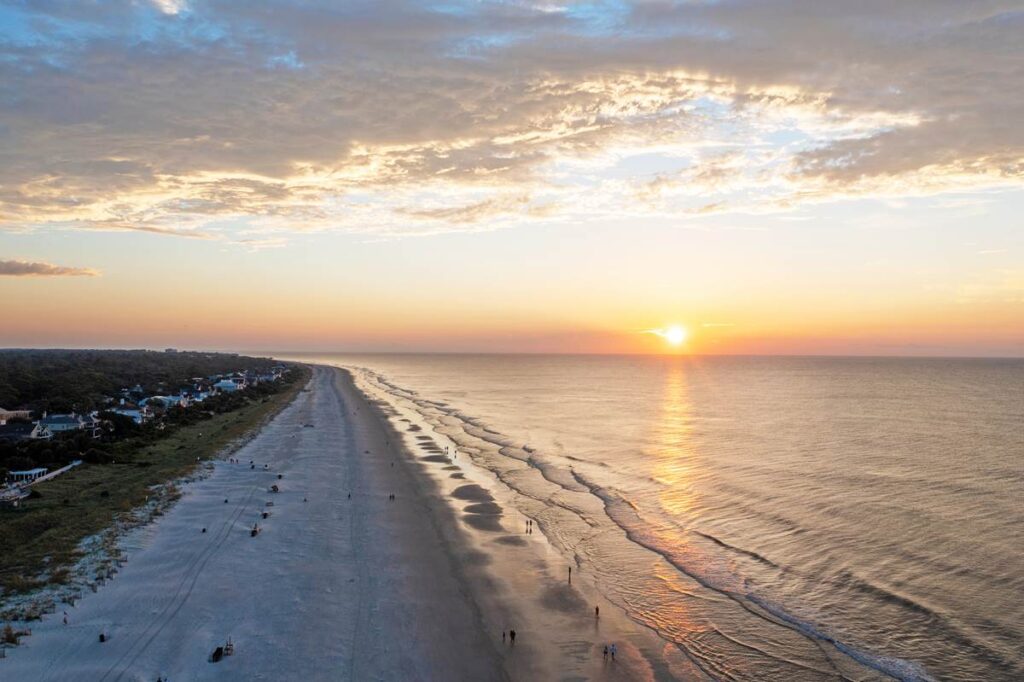 Aerial view of a scenic beach at sunset with calm waves and a colorful sky.