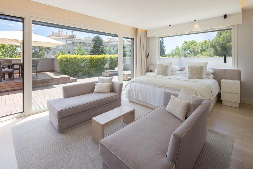 Modern hotel room featuring a cozy bed, stylish seating, large windows, and a balcony with greenery. Ideal for relaxation.