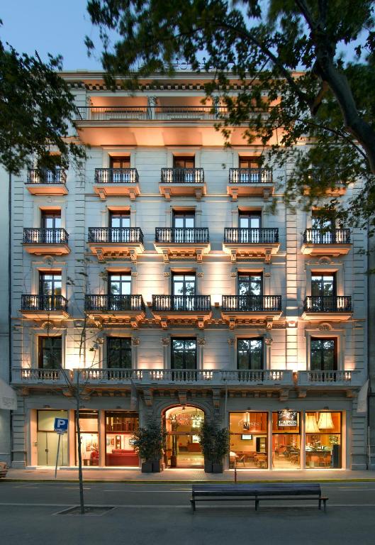 Elegant historic building facade with illuminated balconies and a stylish entrance, surrounded by trees at dusk.