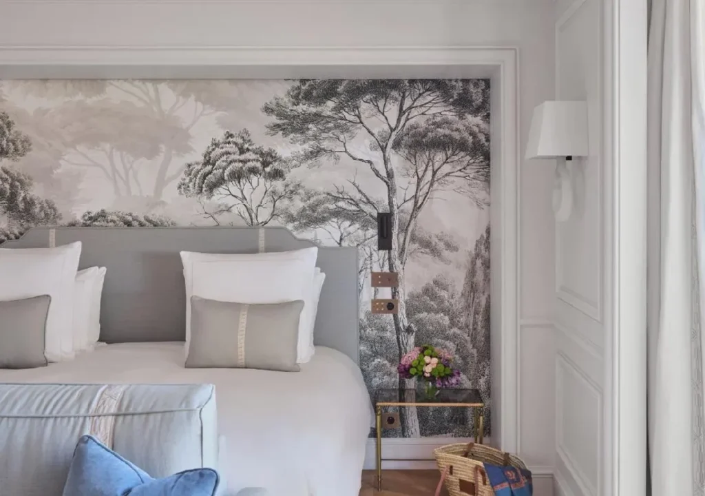 Elegant bedroom featuring a serene tree mural, plush bedding, and a stylish glass side table with flowers.