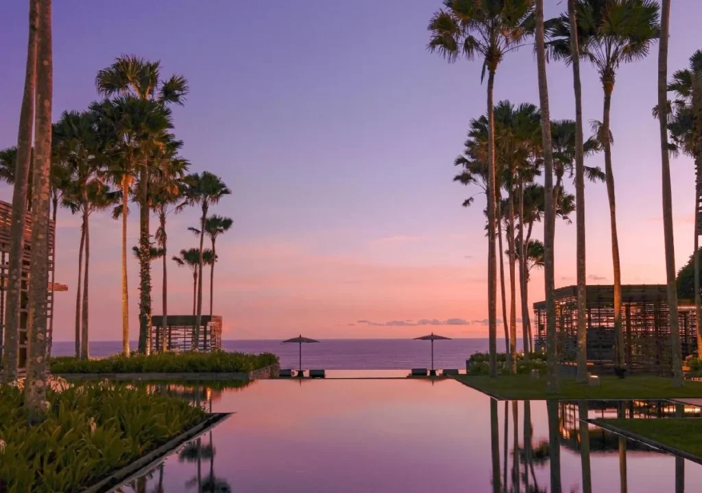 Tranquil sunset view over a serene infinity pool, surrounded by palm trees and ocean waves, creating a paradise atmosphere.