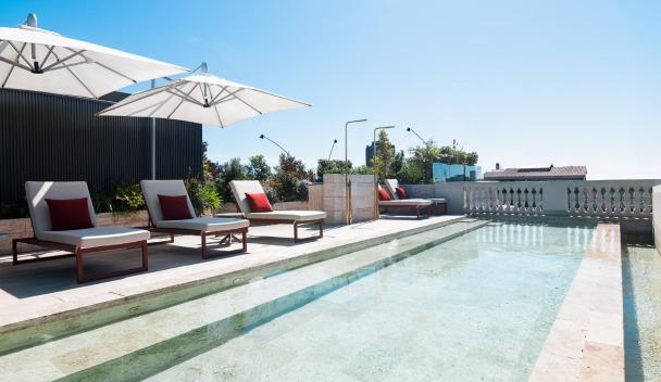 Luxurious outdoor pool area with sun loungers and umbrellas, surrounded by lush greenery and clear blue skies.