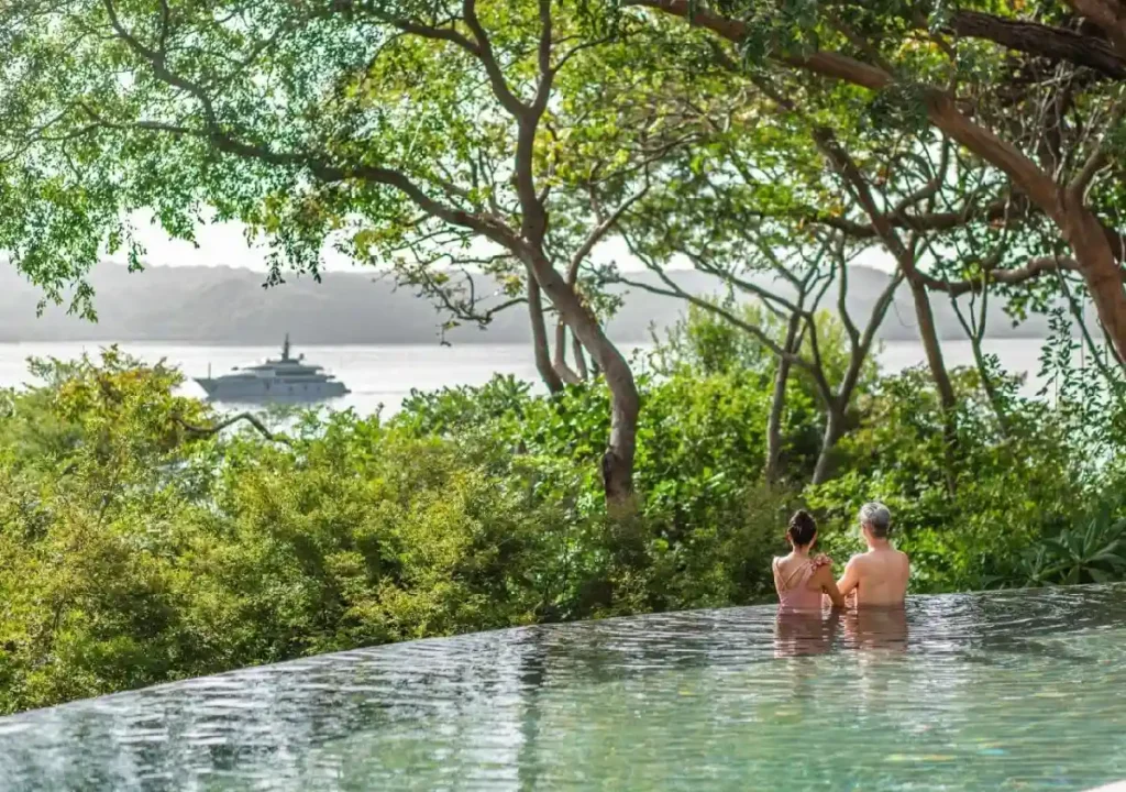 Couple enjoying a serene moment in an infinity pool surrounded by lush greenery and a picturesque view of the ocean.