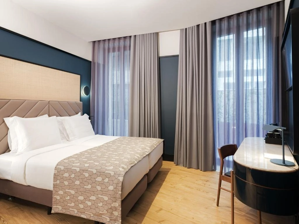 Modern hotel room featuring a comfortable bed, stylish decor, and large windows with sheer curtains. Ideal for relaxation.