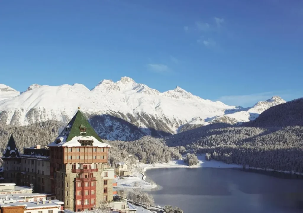 Scenic winter view of snow-covered mountains and lakeside hotel under a clear blue sky. Perfect winter getaway destination.