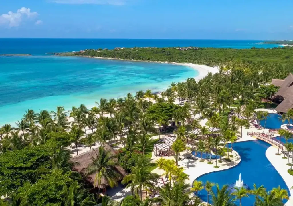 A stunning aerial view of a tropical resort featuring turquoise waters, palm trees, and poolside relaxation areas.