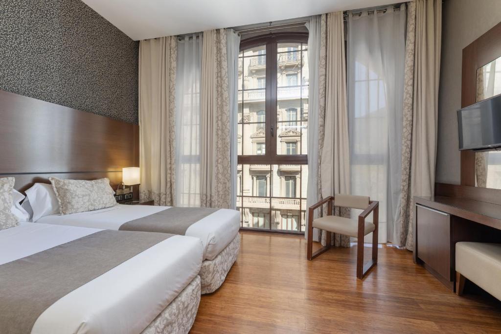 Cozy hotel room with two beds, large windows, and modern decor, featuring wood flooring and stylish furnishings.