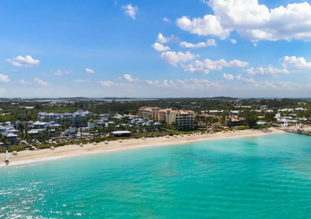 Aerial view of a serene beach with turquoise waters and resorts under a blue sky with fluffy clouds. Perfect vacation spot.