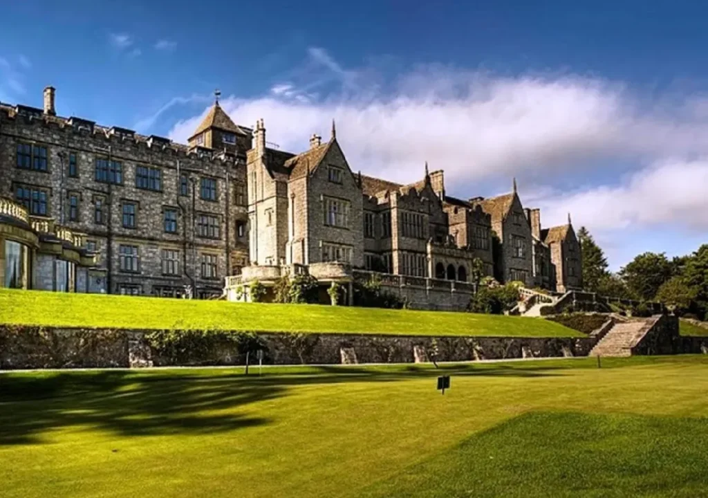 Historic stone building surrounded by lush green lawns under a blue sky with clouds, ideal for travelers seeking elegance.
