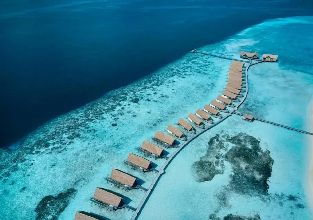 Aerial view of luxurious overwater bungalows surrounded by vibrant turquoise waters in a tropical paradise.