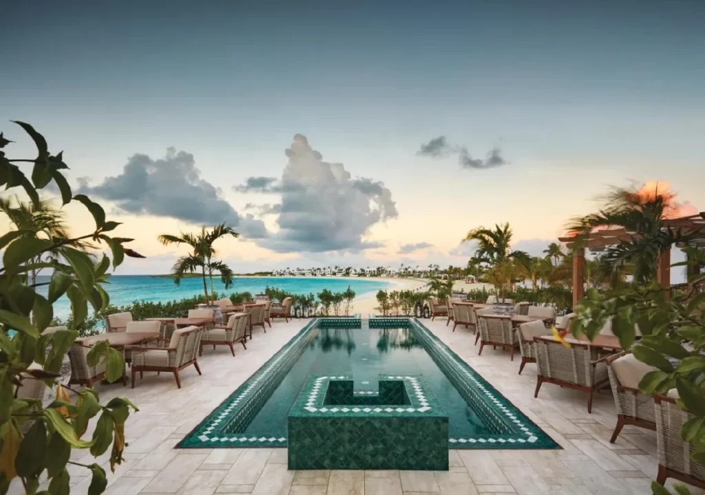 Scenic oceanfront dining area with a pool and palm trees, perfect for a relaxing getaway at a luxury resort.