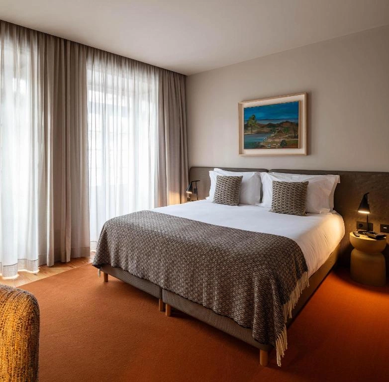 Modern hotel room featuring a cozy queen bed, natural light, and elegant decor for a relaxing stay.