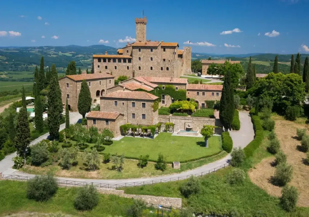 Aerial view of a historic castle surrounded by lush greenery and farmland under a clear blue sky. Ideal for promotions.