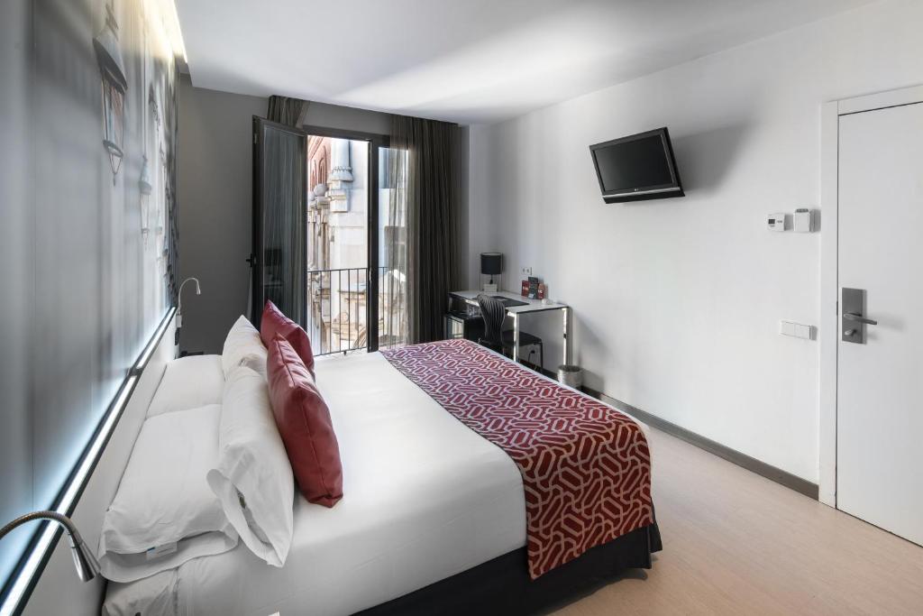 Modern hotel bedroom featuring a queen-sized bed, work desk, and balcony with city views. Ideal for a relaxing stay.